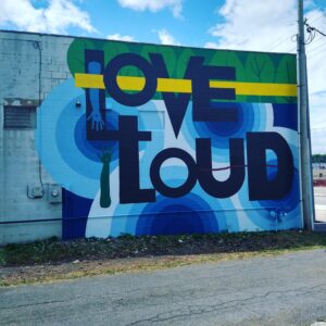 Mural on the side of a square building with shades of blue in the background and black block letters that read Love Out Loud